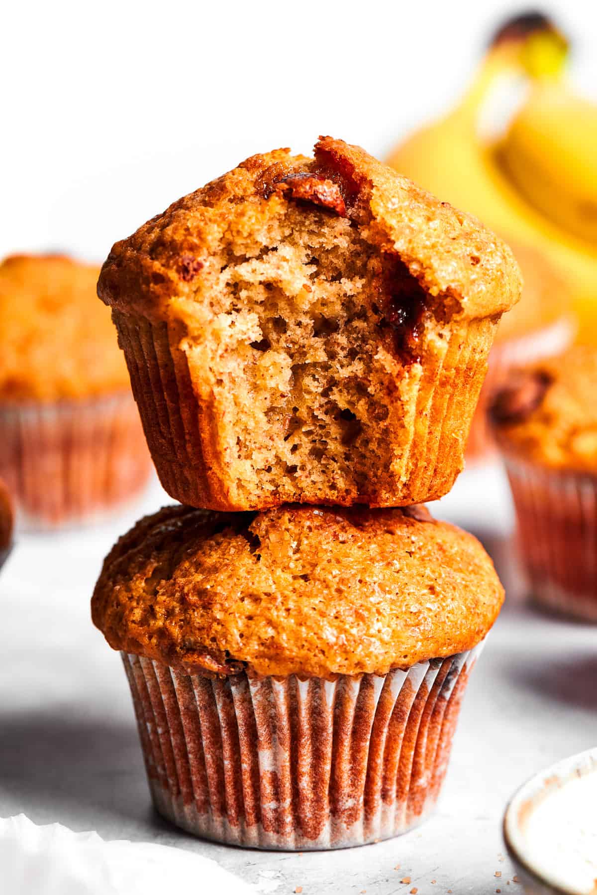 A banana muffin bitten into stands on top of a whole banana muffin.