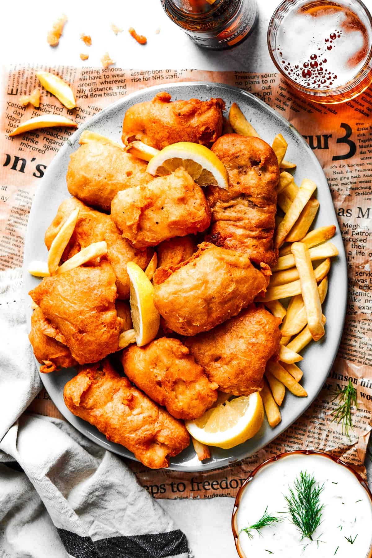 Overhead photo of battered fried shrimp served on a platter with fries, with bottles of beer set next to it and also a bowl of tartar sauce.