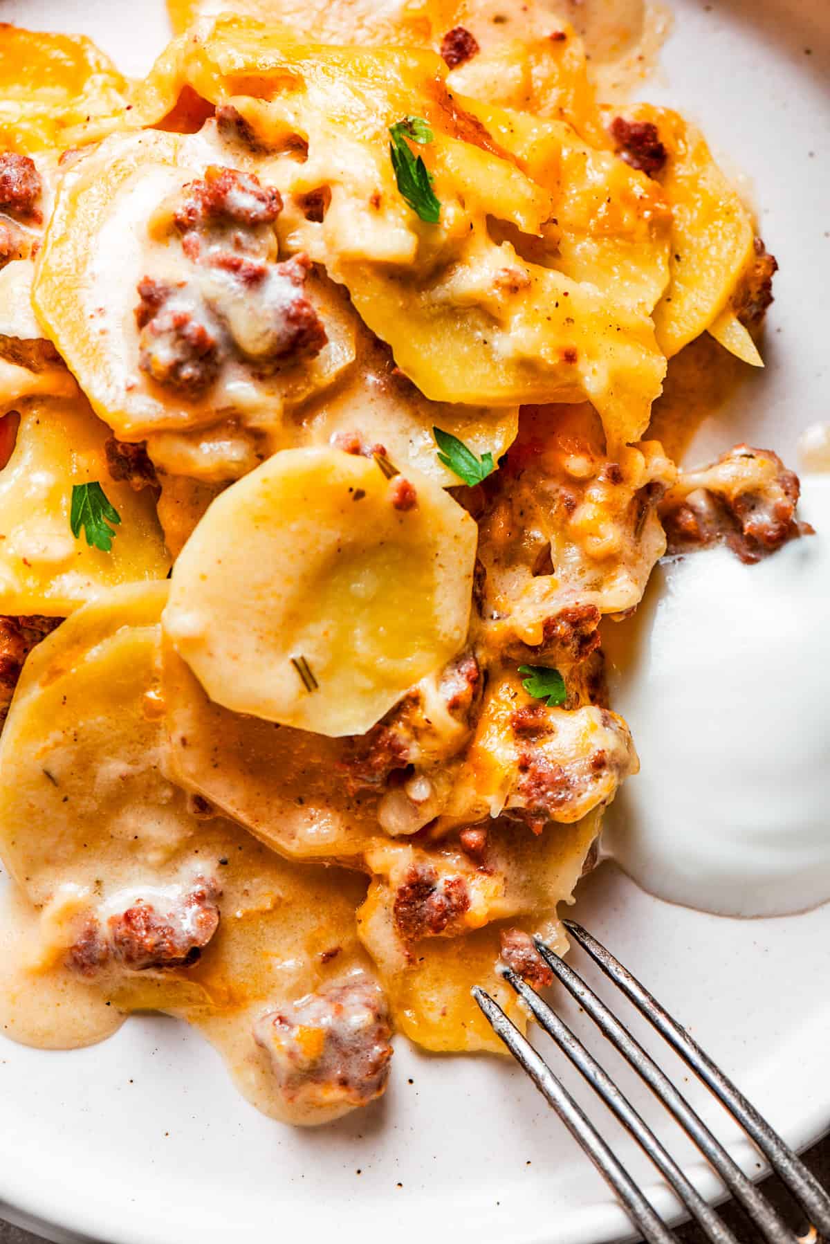 Close-up image of cooked sliced potatoes and ground beef served on a dinner plate with a fork set next to the food.