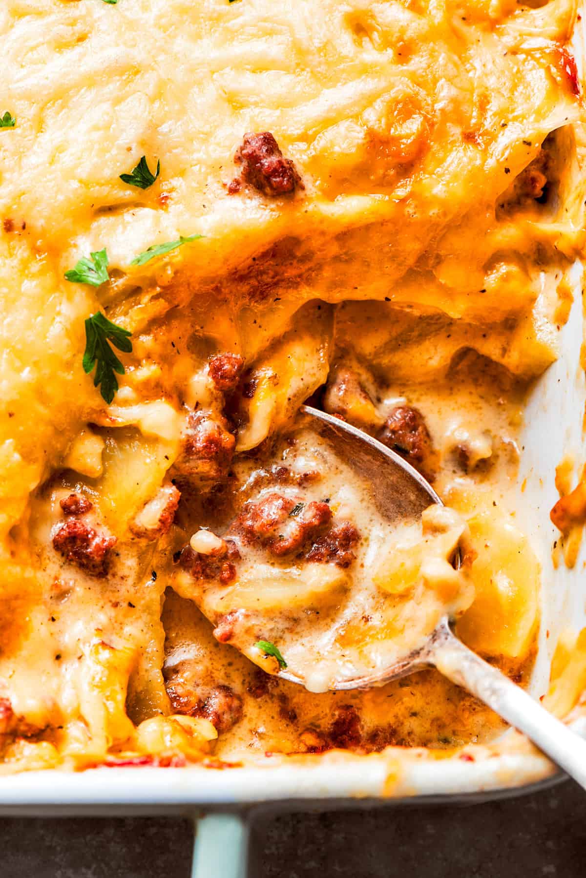 A spoon mixing through a casserole with ground beef and potatoes.