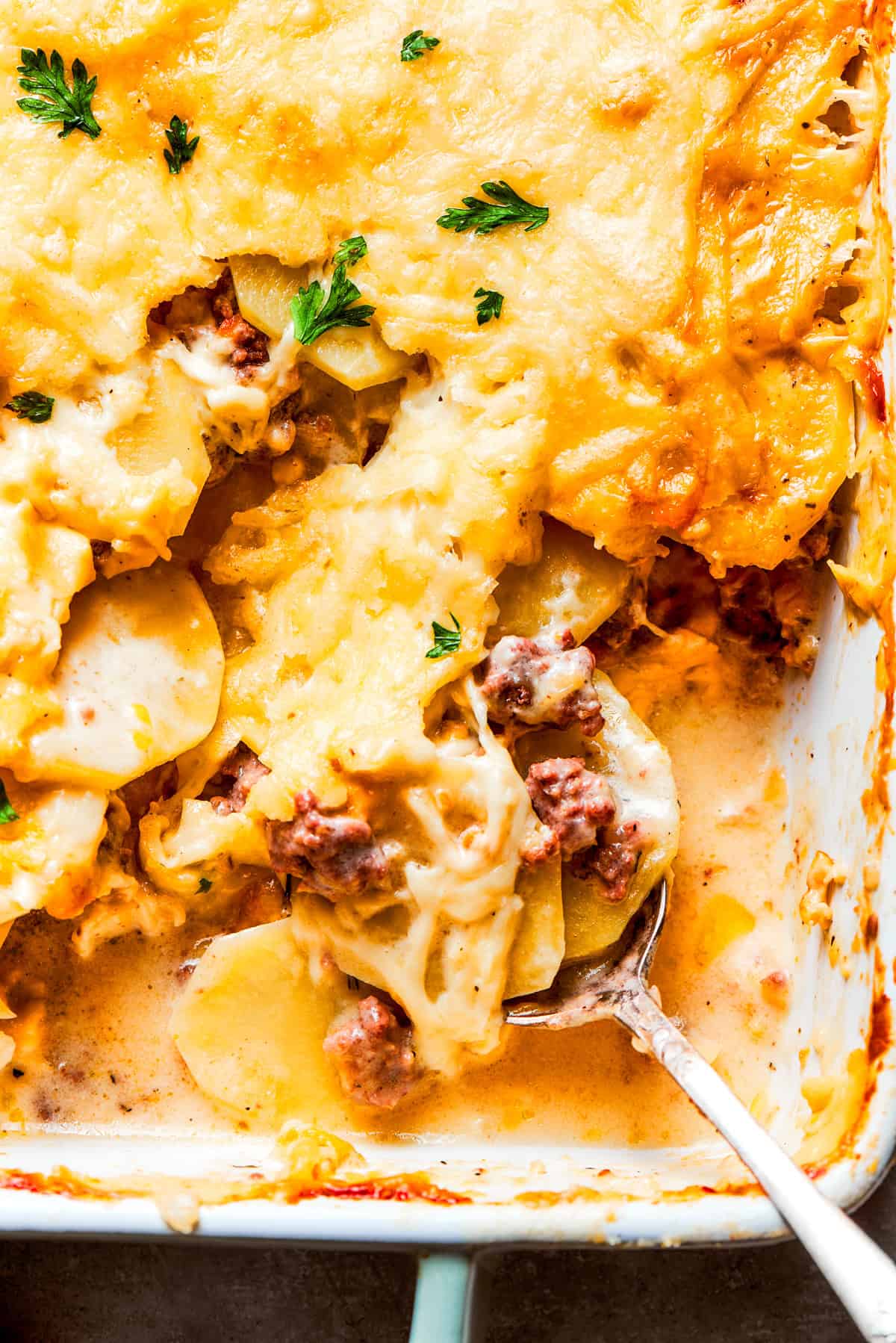 Up close photo of a spoon mixing through a casserole with ground beef and potatoes.