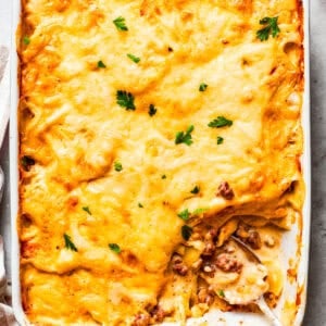 Overhead image of hamburger potato casserole in a baking dish, with a serving of it missing from the corner.