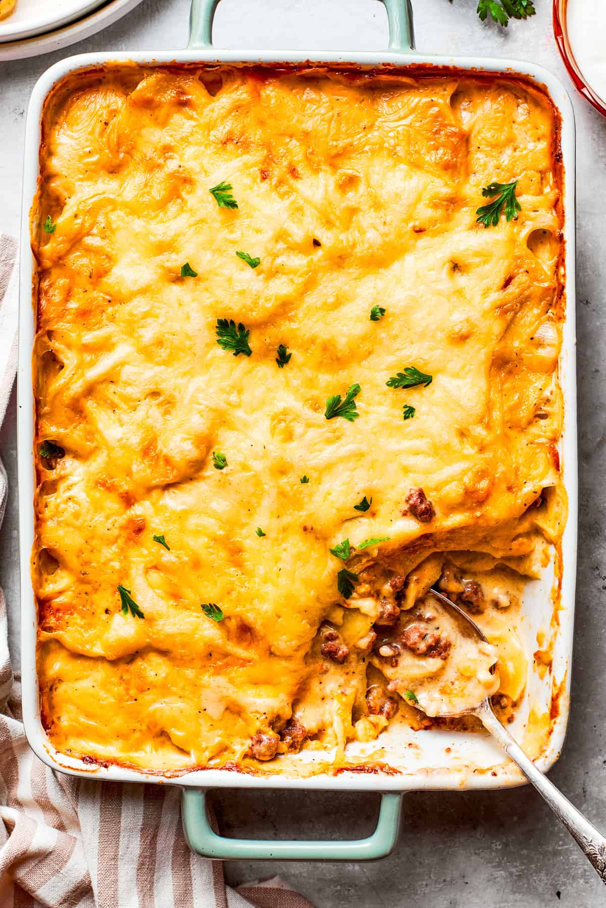 Overhead image of hamburger potato casserole in a baking dish, with a serving of it missing from the corner.