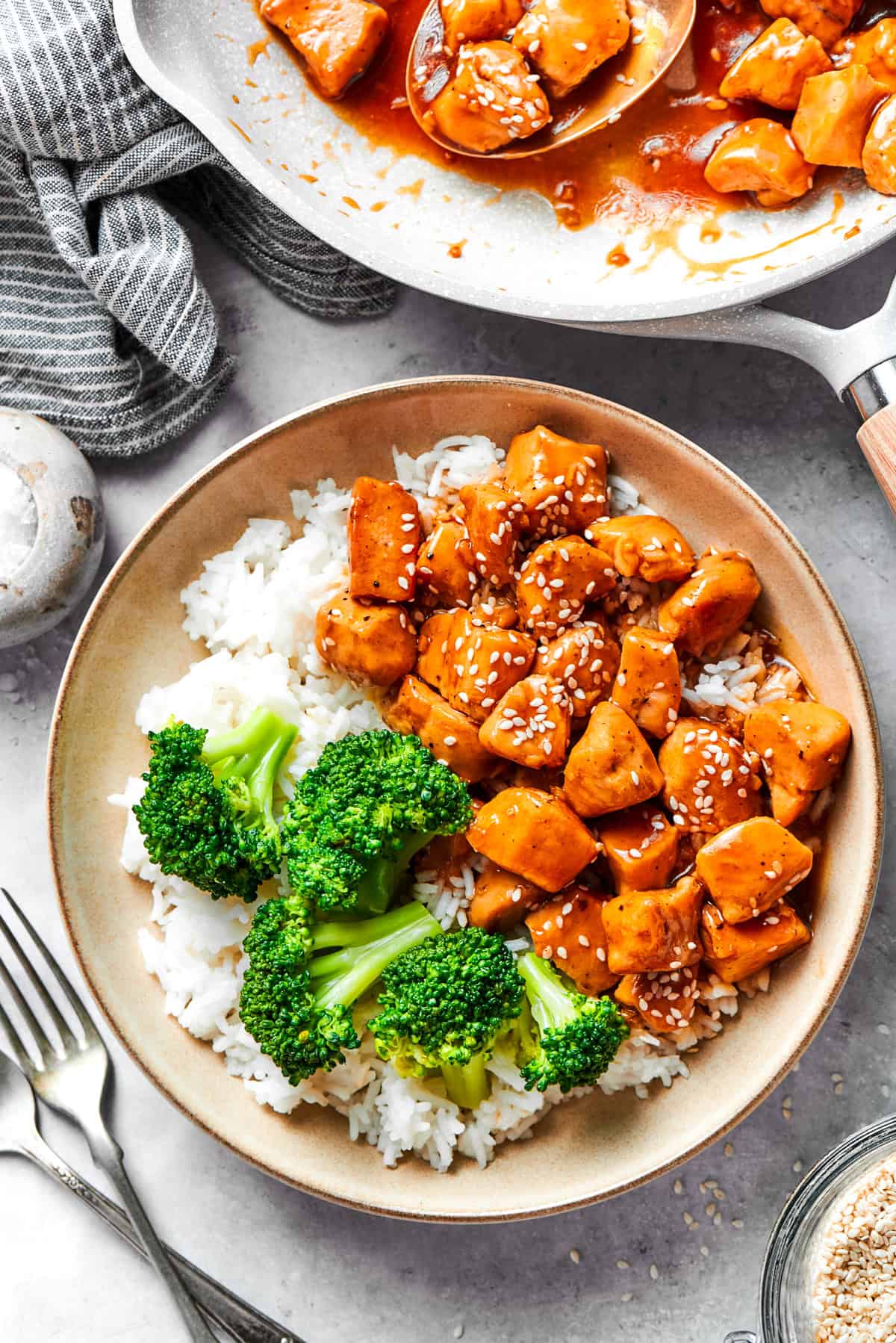 A bowl of rice is topped with teriyaki chicken and broccoli with more teriyaki chicken in the background.