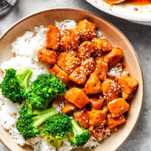 Teriyaki chicken pieces served over rice in a bowl with a side of broccoli.