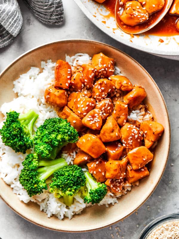 Teriyaki chicken pieces served over rice in a bowl with a side of broccoli.