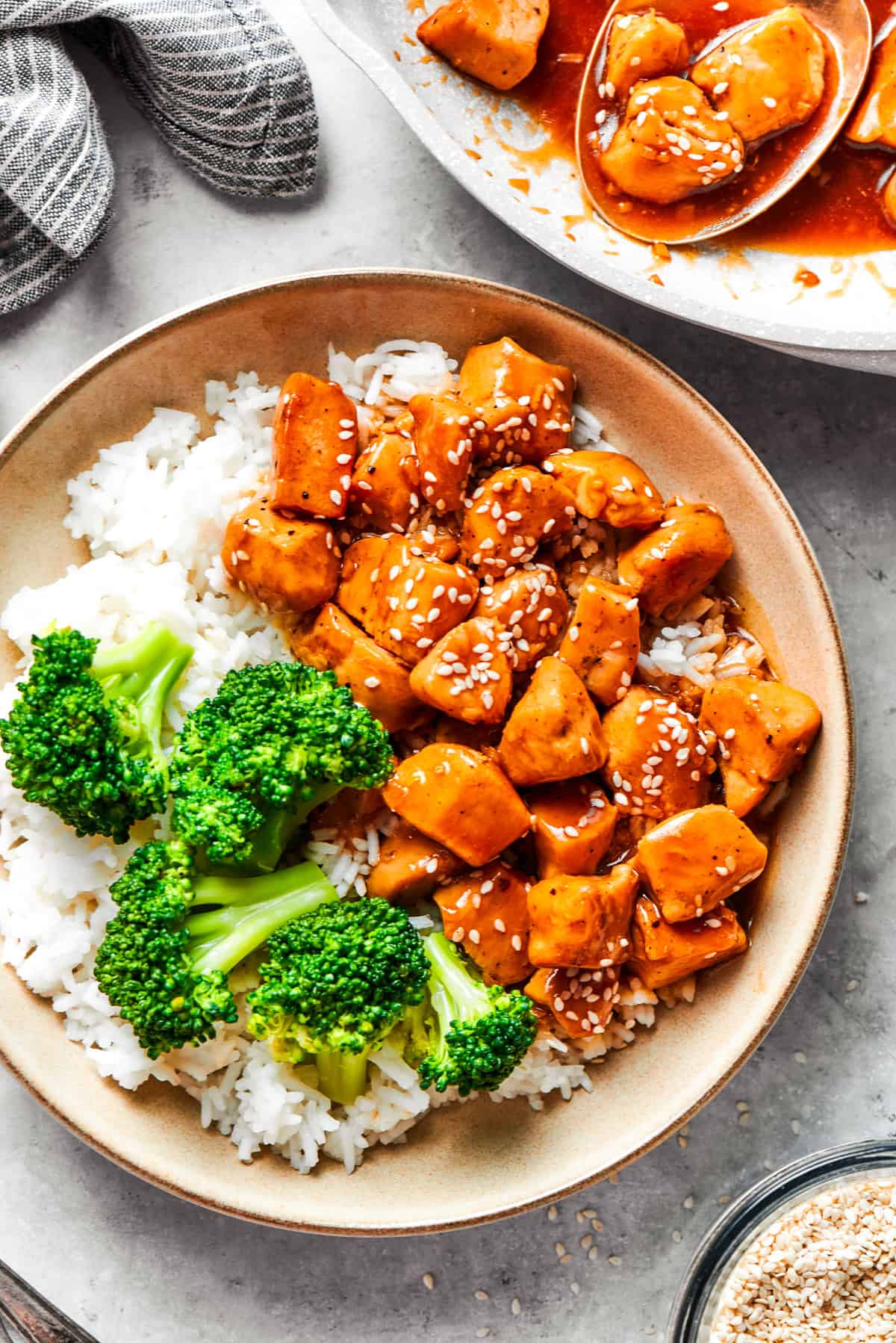 Teriyaki chicken pieces served over rice in a bowl with a side of broccoli.