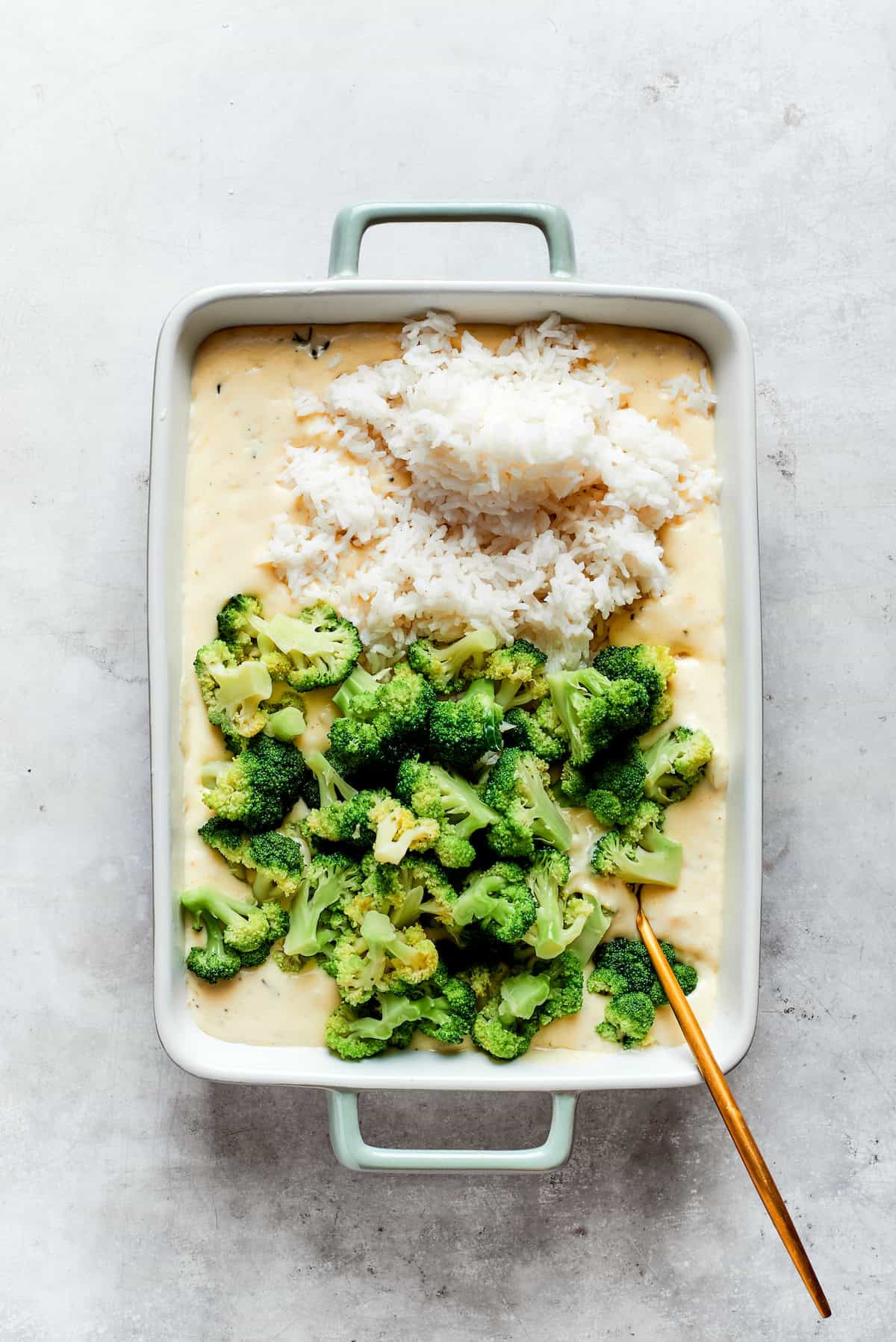 A baking pan with cheese sauce, broccoli, and rice.