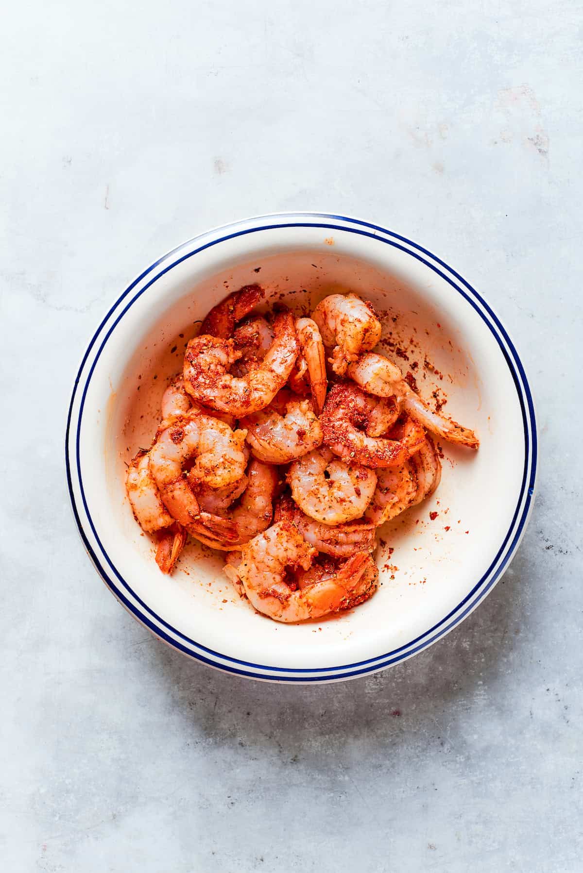 Shrimp is mixed with spices in a bowl.