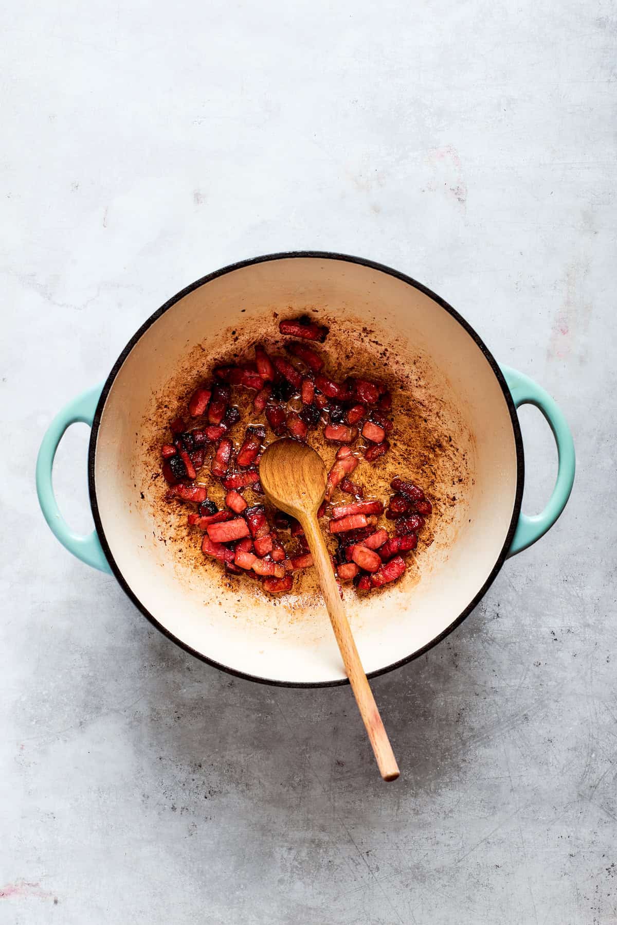 A spoon stirs chopped bacon in a pot.