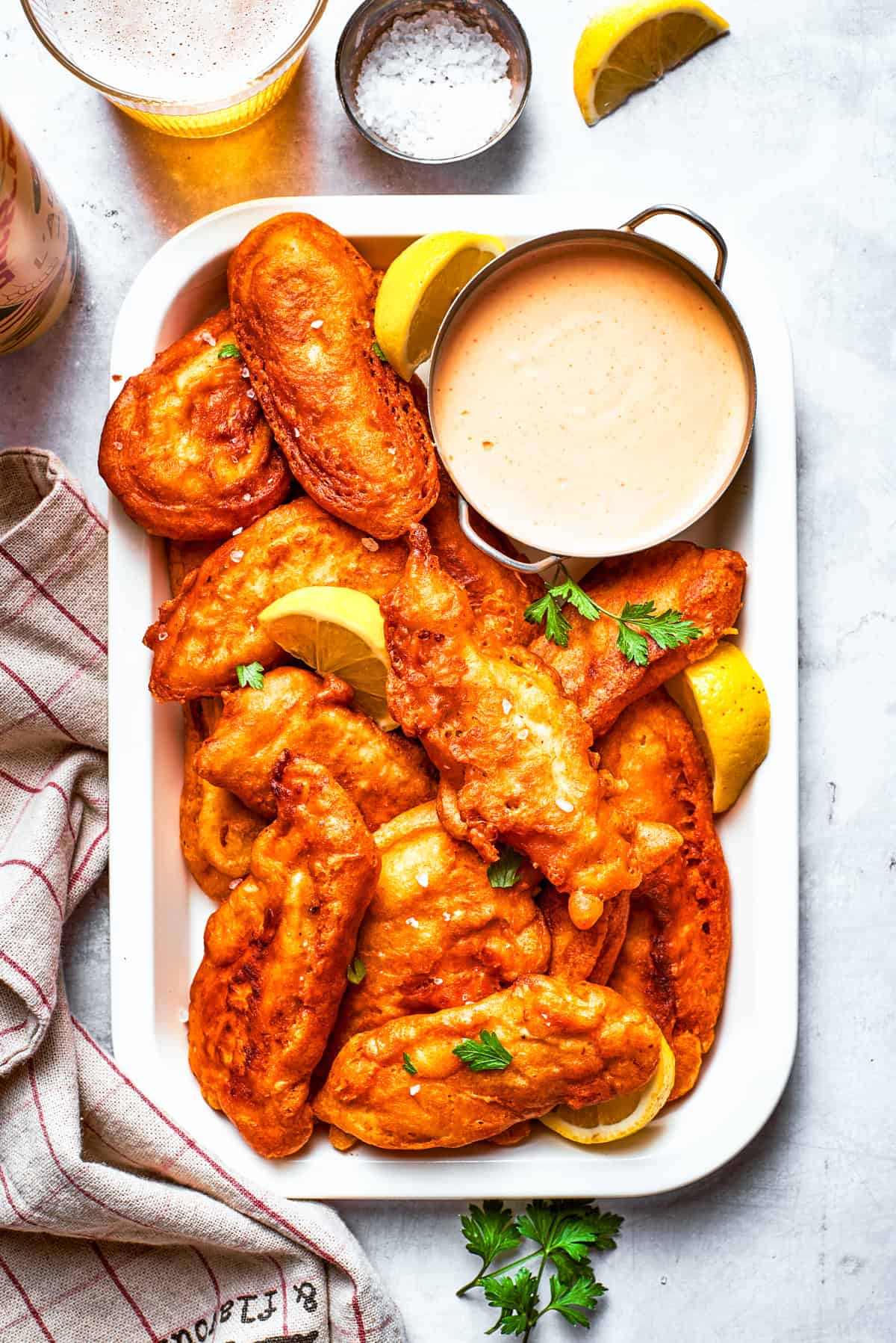 Pieces of beer battered chicken arranged on a rectangular serving plate with a bowl of dipping sauce.