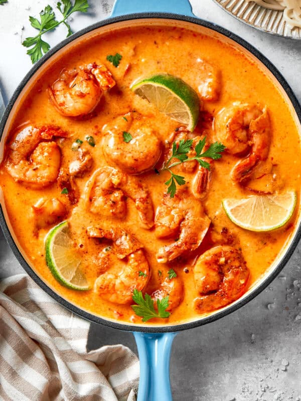 A skillet of cooked shrimp in tomato sauce. There are lime wedges arranged all around the shrimp.