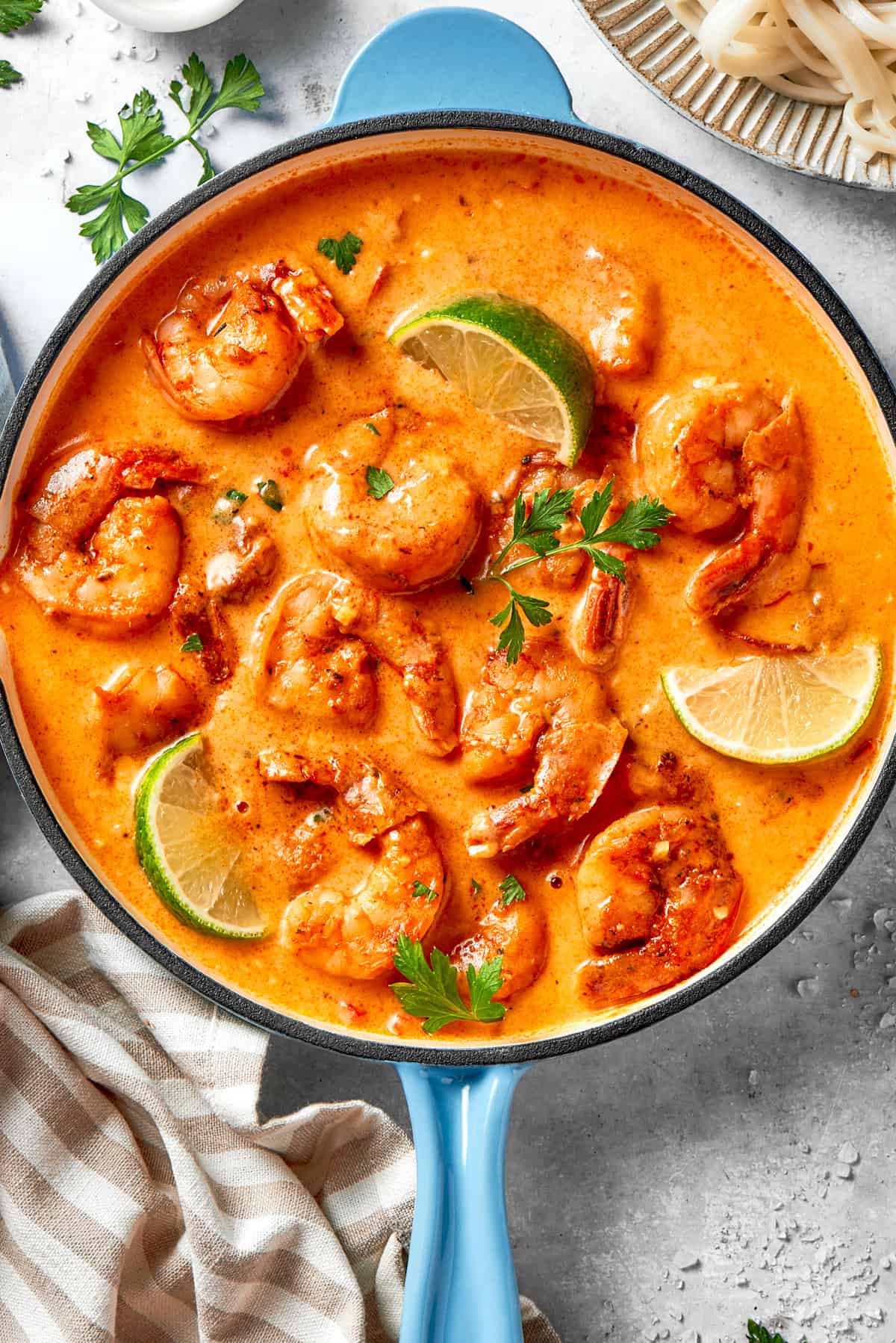 A skillet of cooked shrimp in tomato sauce. There are lime wedges arranged all around the shrimp.