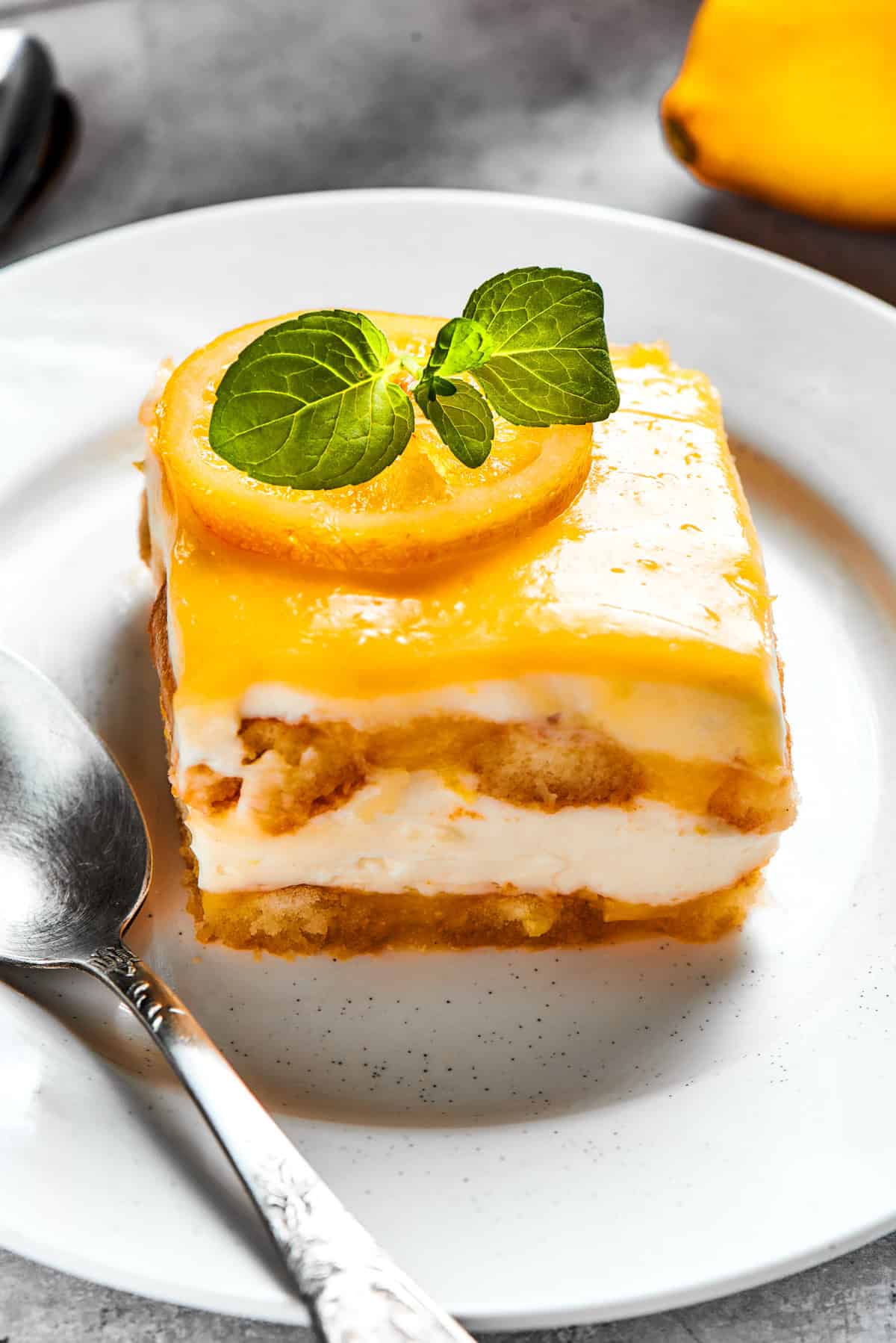 A square of lemon tiramisu on a white plate and topped with fresh basil.