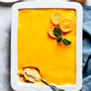 A serving spoon is digging into the corner of a pan of lemon tiramisu.