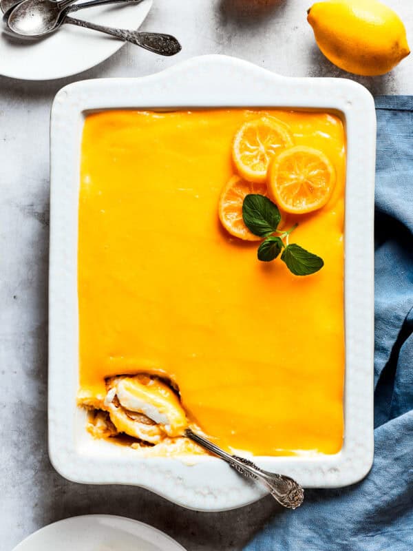 A serving spoon is digging into the corner of a pan of lemon tiramisu.