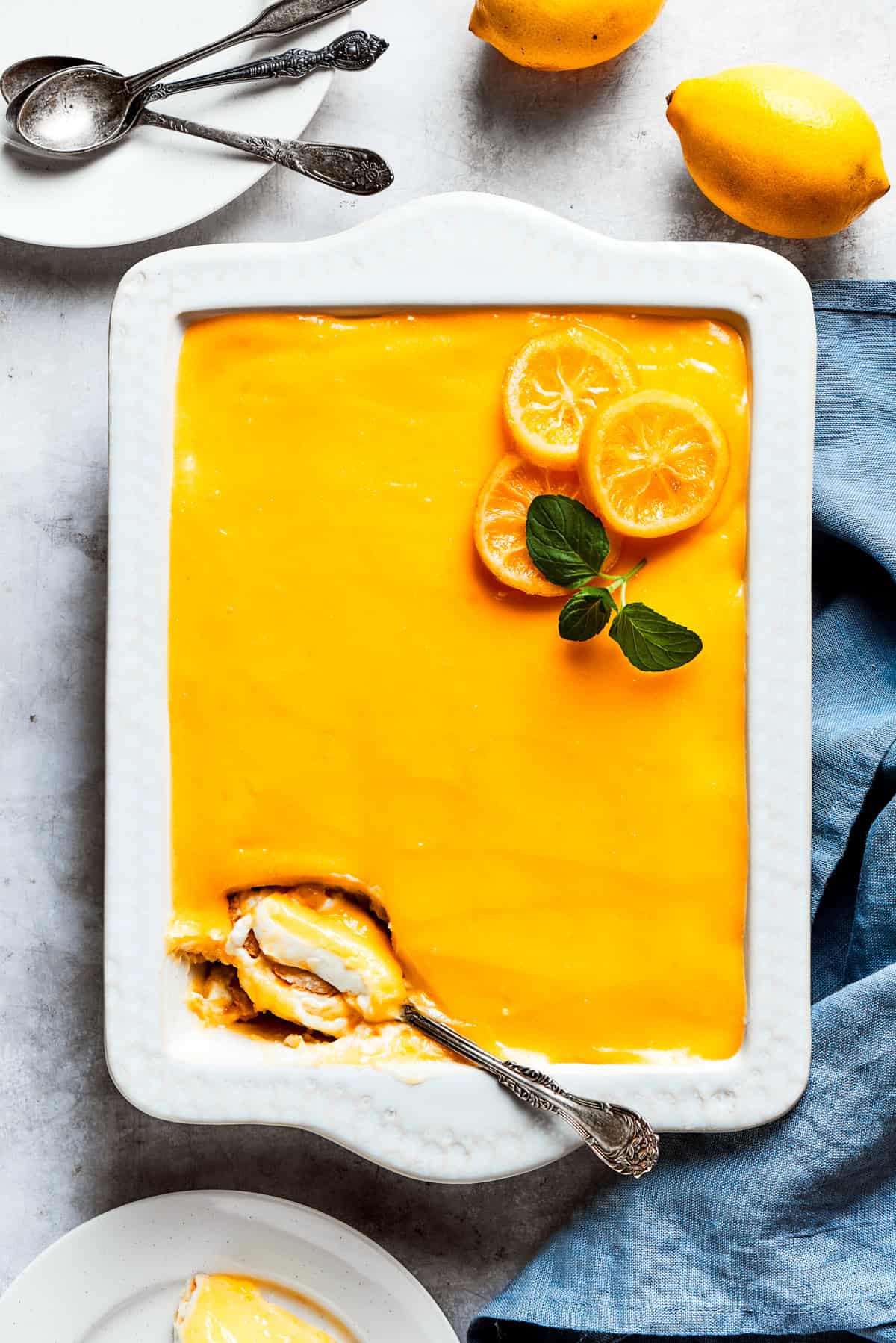 A serving spoon is digging into the corner of a pan of lemon tiramisu.