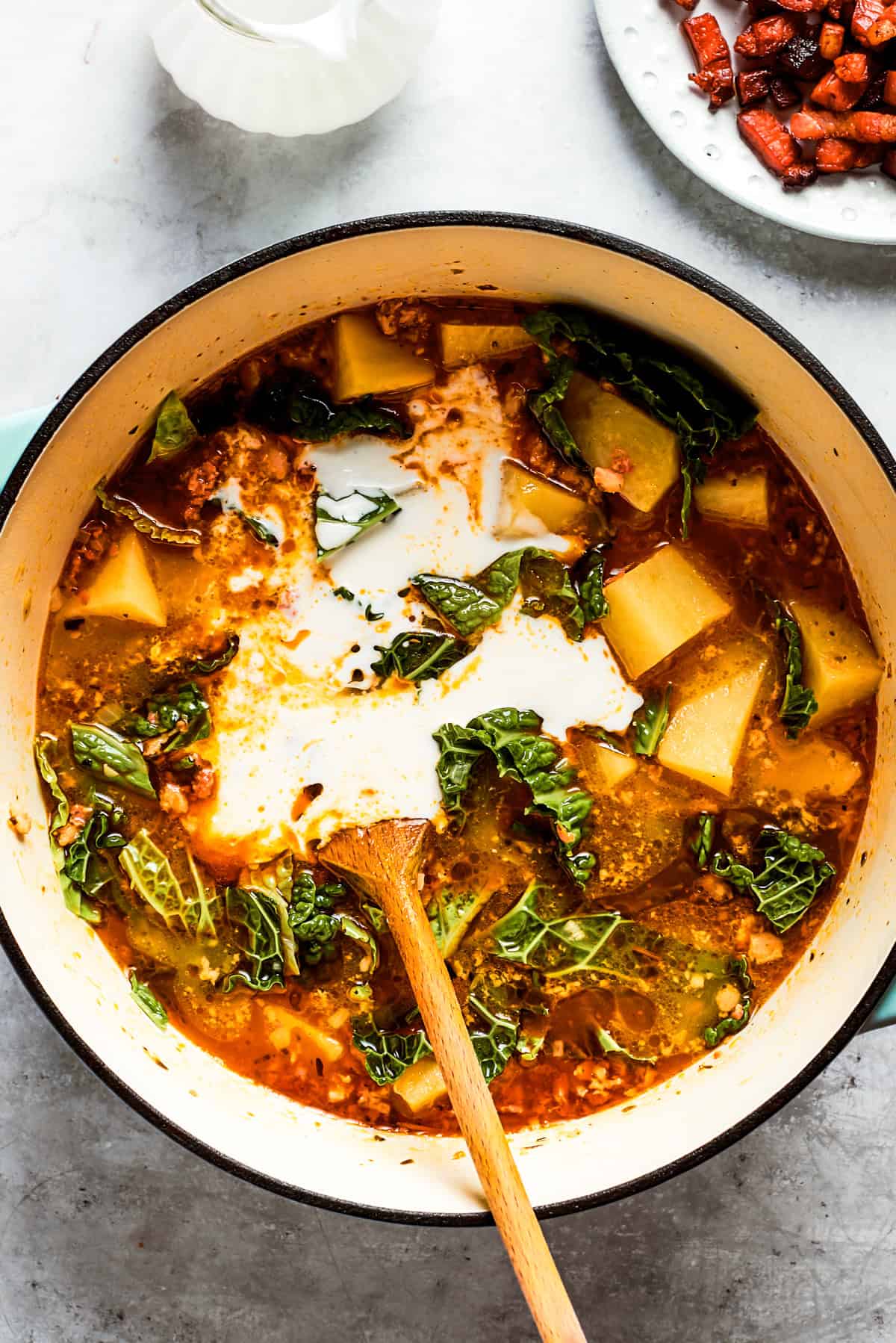 Stirring heavy cream into a pot of soup with diced potatoes.