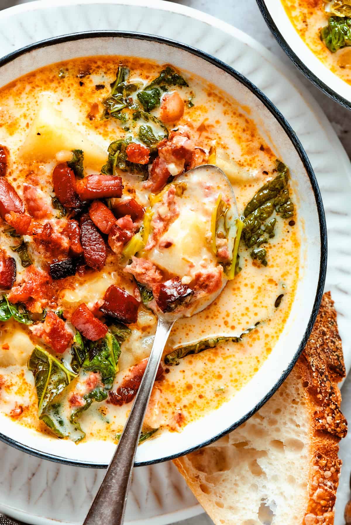 Close-up shot of Zuppa Toscana served in a bowl with a spoon placed inside it.