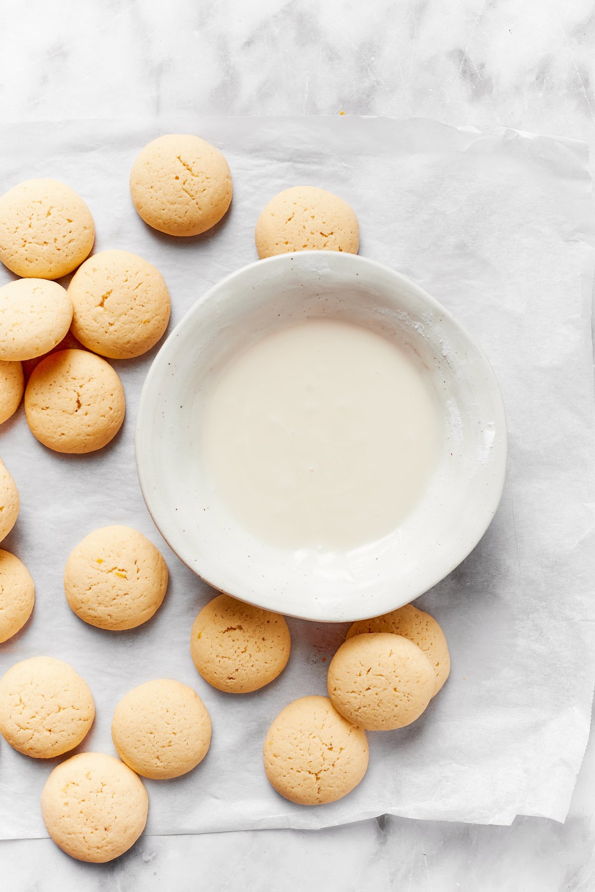 A bowl of icing surrounded by anginetti cookies.