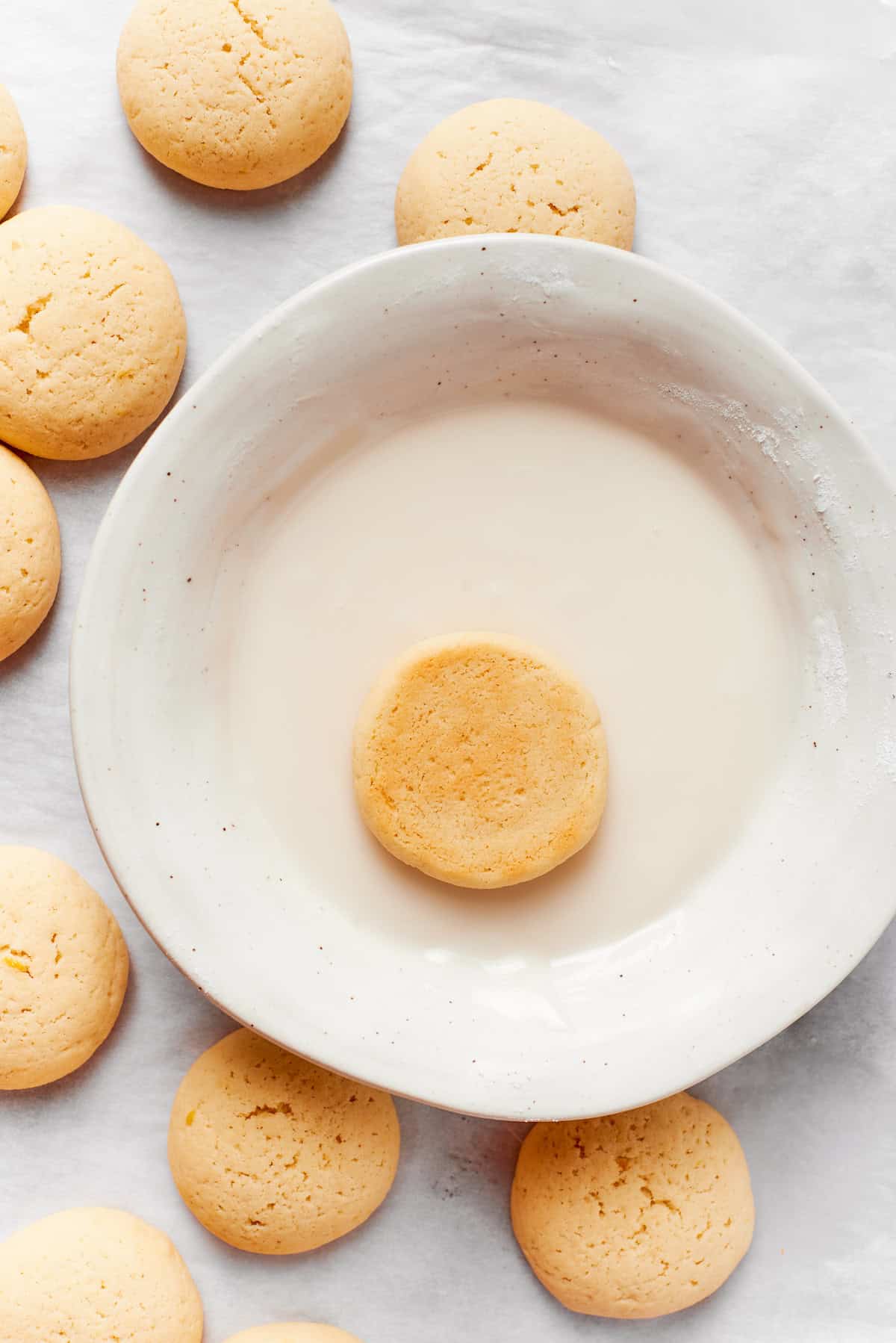 An anginetti cookie is dipped in a bowl of icing.