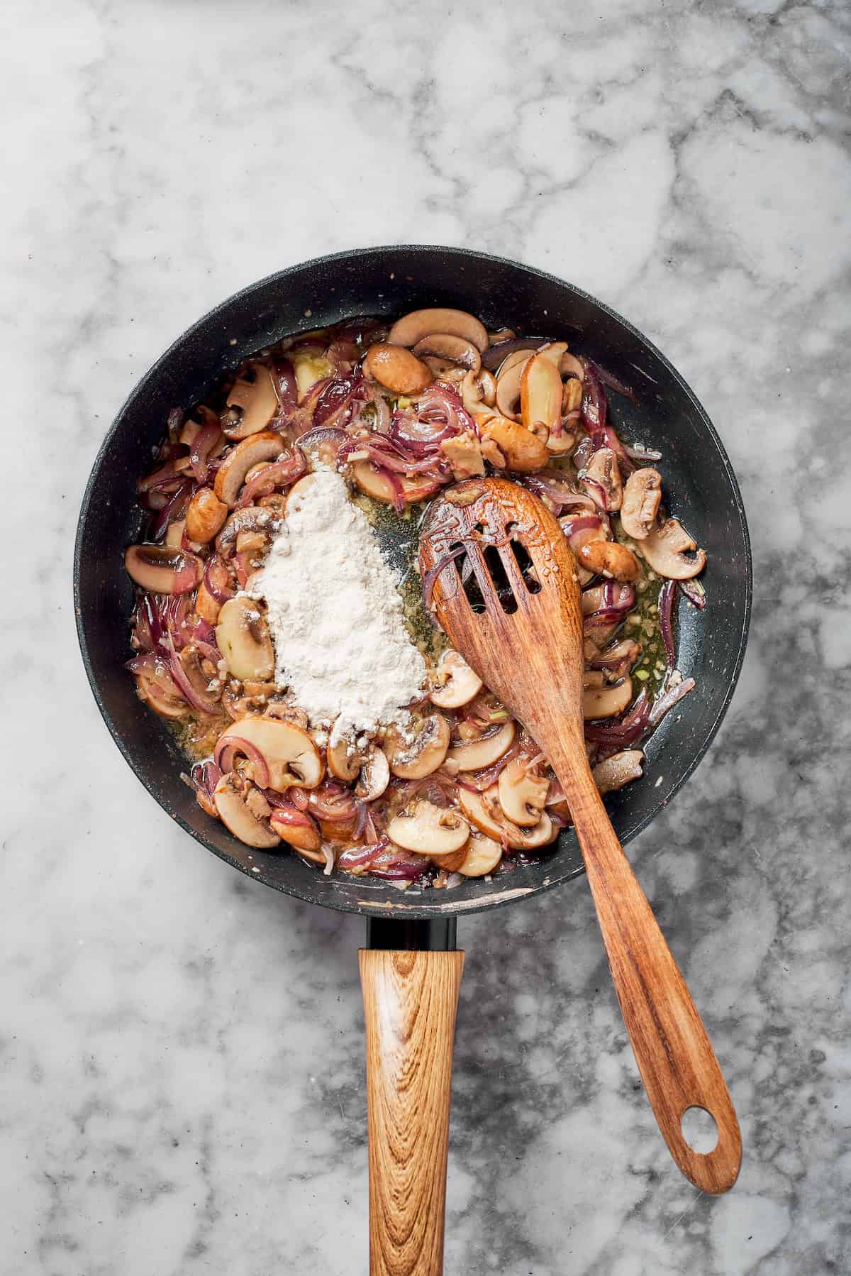 Adding flour to cooked mushrooms in a pan.