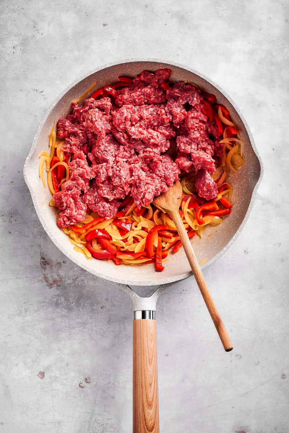 Adding ground beef to onions and peppers in a skillet.