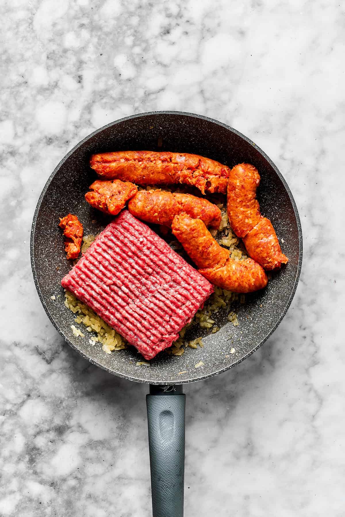 Adding ground beef and sausage to the skillet.