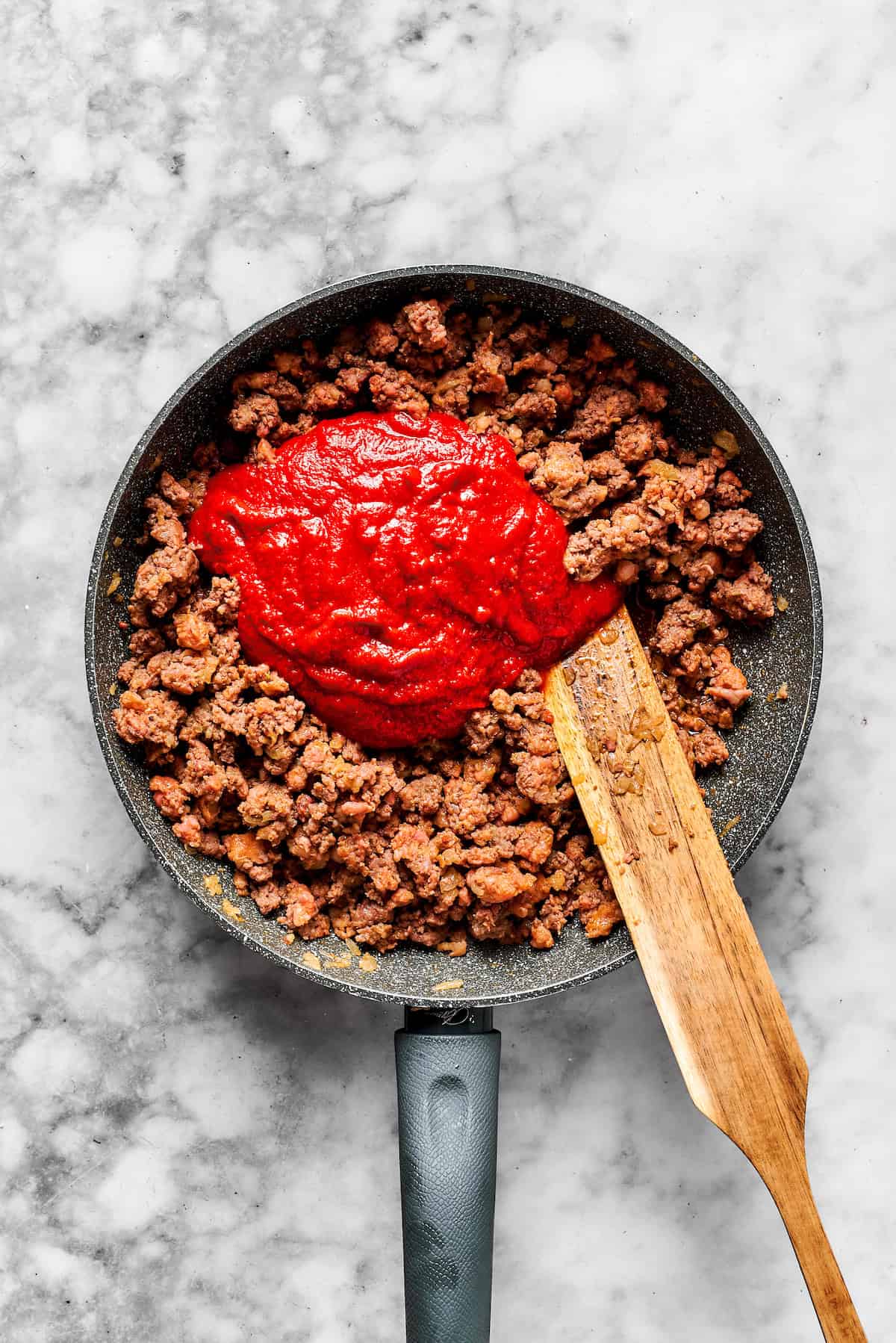 Adding pasta sauce to a skillet with cooked meat.