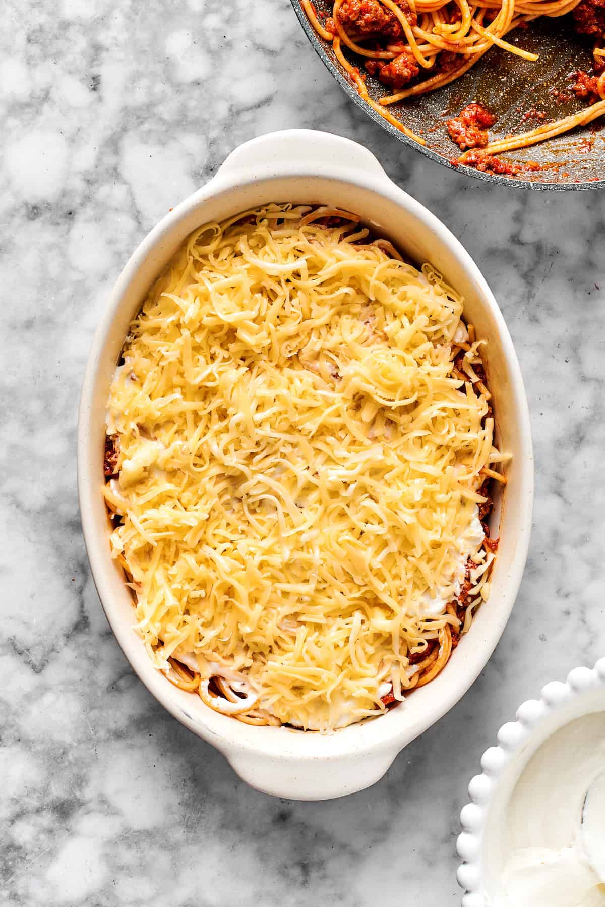 Adding a layer of shredded cheese on top of spaghetti in a 9x13 dish.