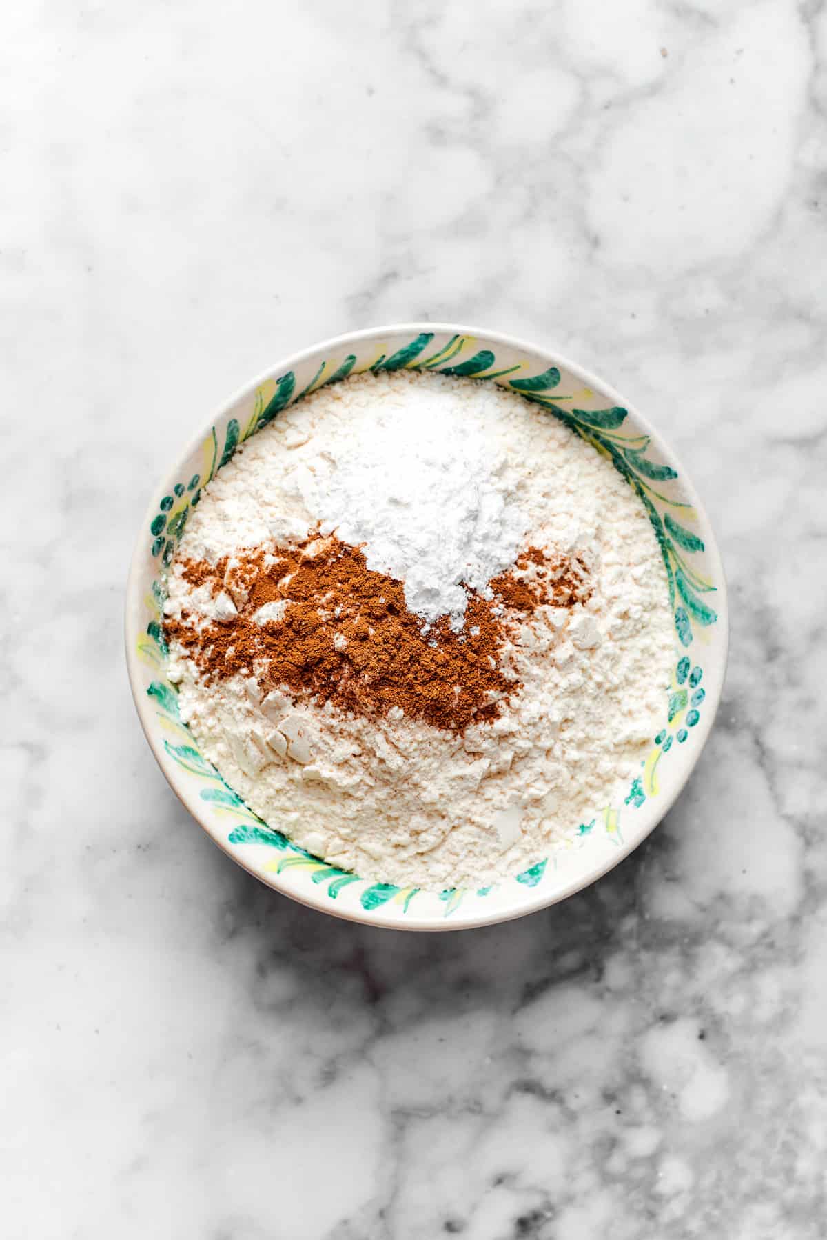 Spices and baking powder are mixed with flour in a bowl.