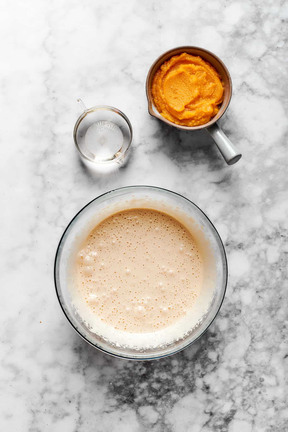 A bowl of muffin batter with a cup of pumpkin puree.