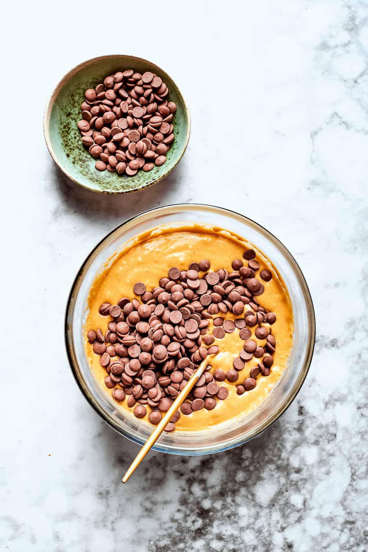 Chocolate chips are added to a bowl of pumpkin muffin batter.