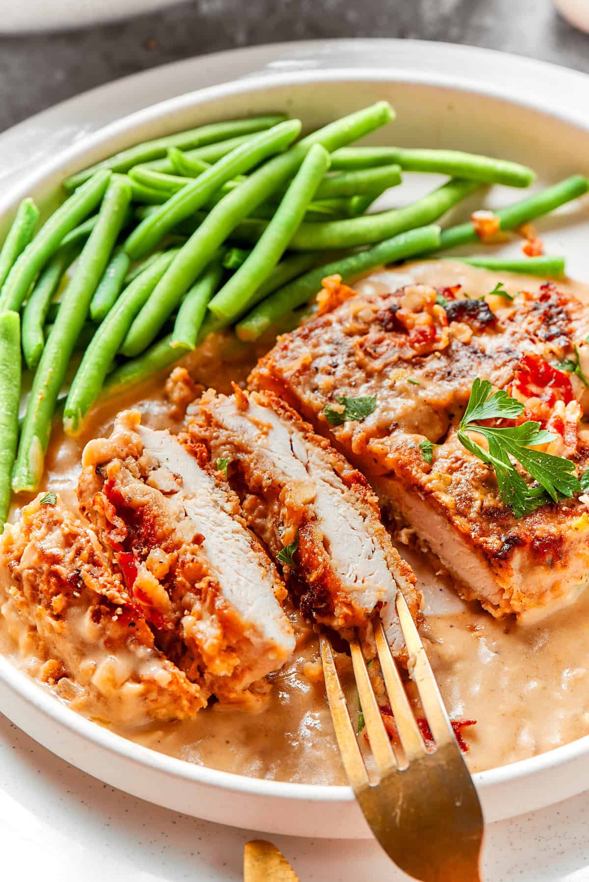 A piece of smothered chicken sliced on a plate with green beans.