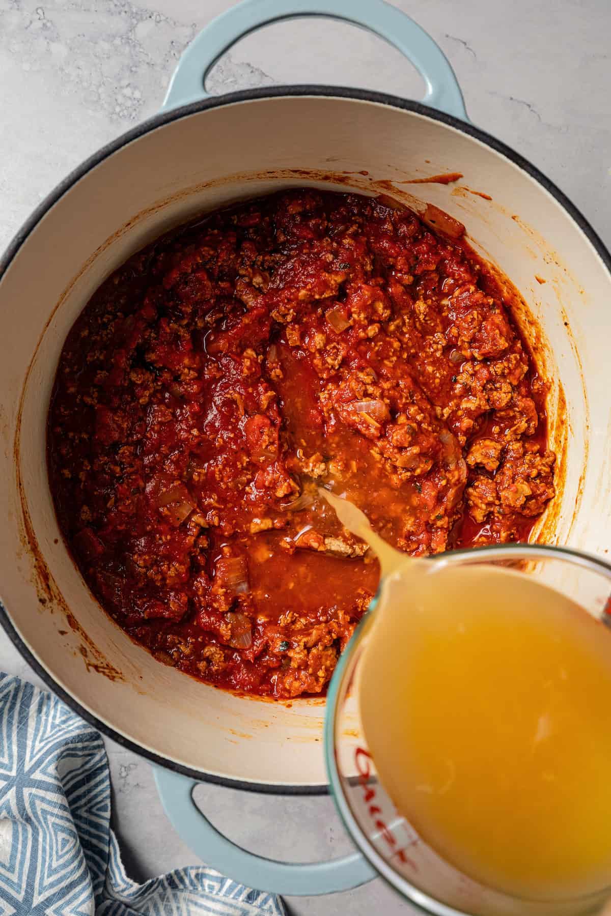 Chicken broth being poured over the other turkey chili ingredients in a pot.