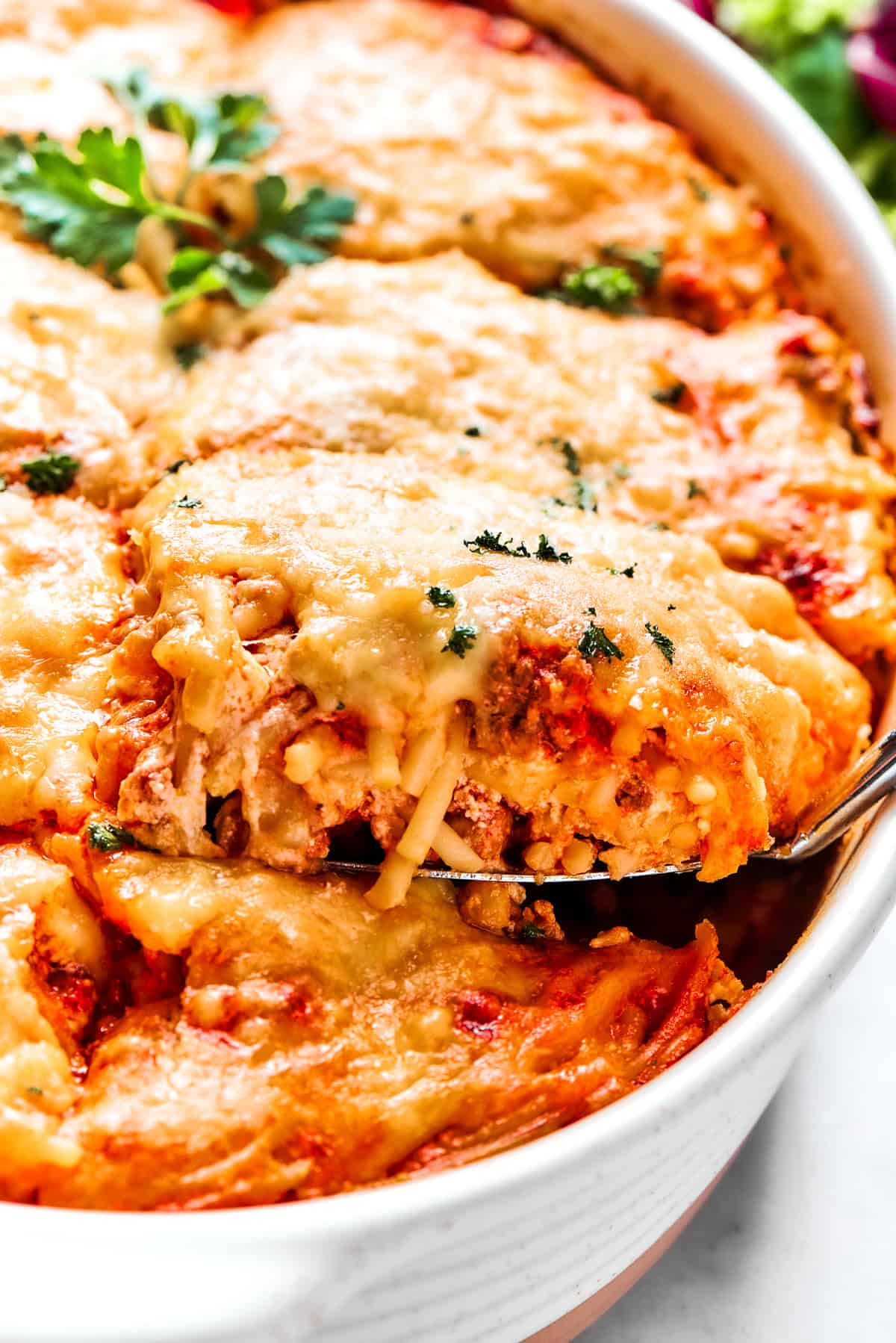 Spooning out baked spaghetti from a casserole dish.