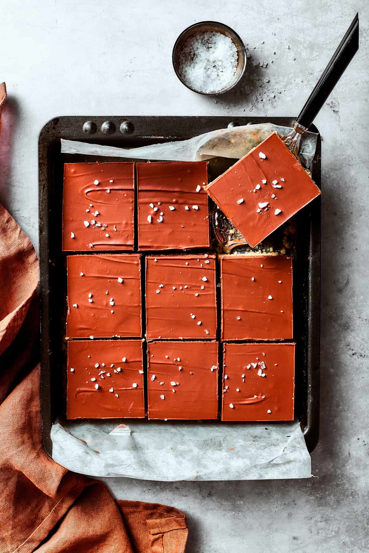 A serving utensil lifts out a square of millionaire bar from a pan.