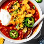 Overhead image of a bowl of turkey chili garnished with sour cream, jalapeños, and corn chips.