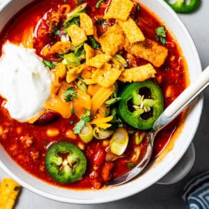 Overhead image of a bowl of turkey chili garnished with sour cream, jalapeños, and corn chips.