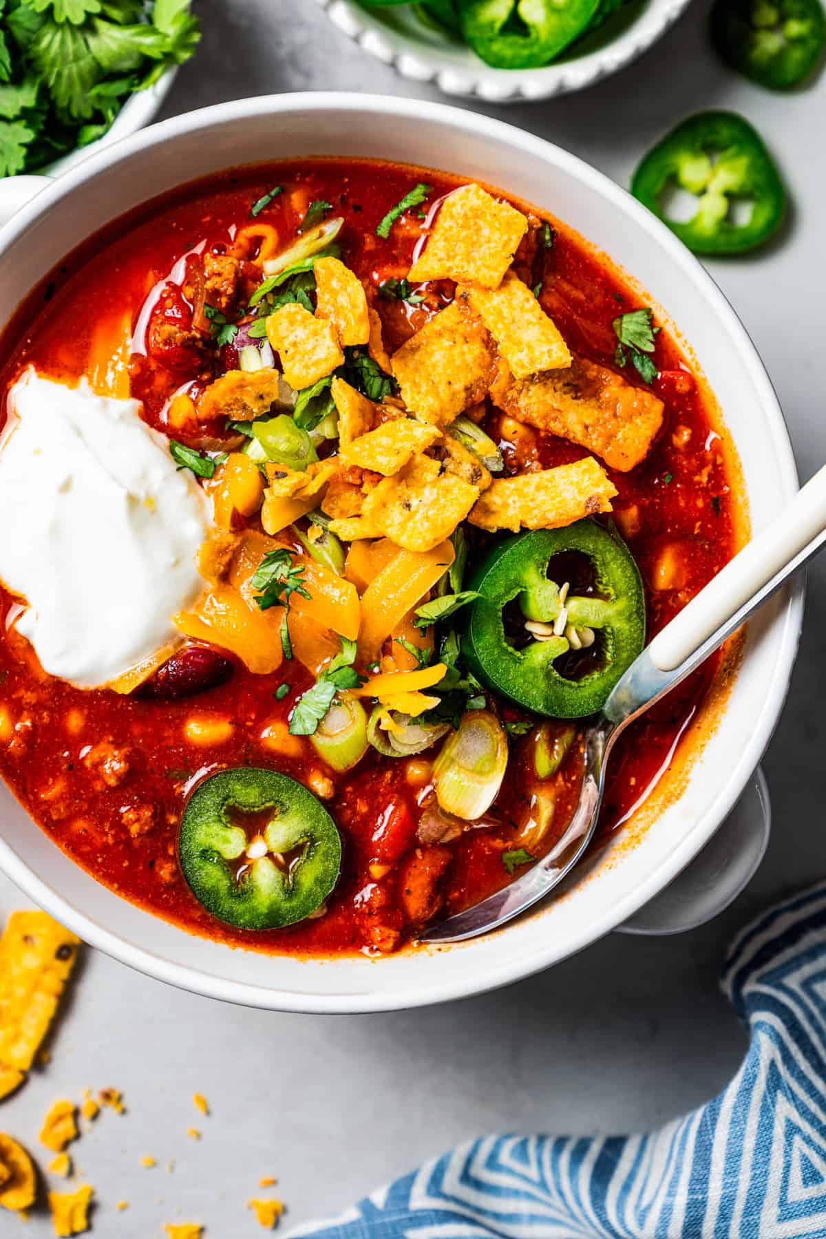 Overhead image of a bowl of turkey chili garnished with sour cream, jalapeños, and corn chips.