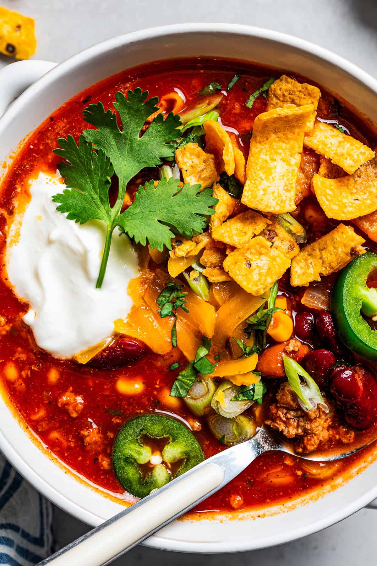 Overhead close up view of a bowl of turkey chili garnished with sour cream, jalapeños, and corn chips.