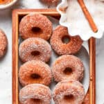 A tray of baked apple cider donuts next to a bowl of sugar.