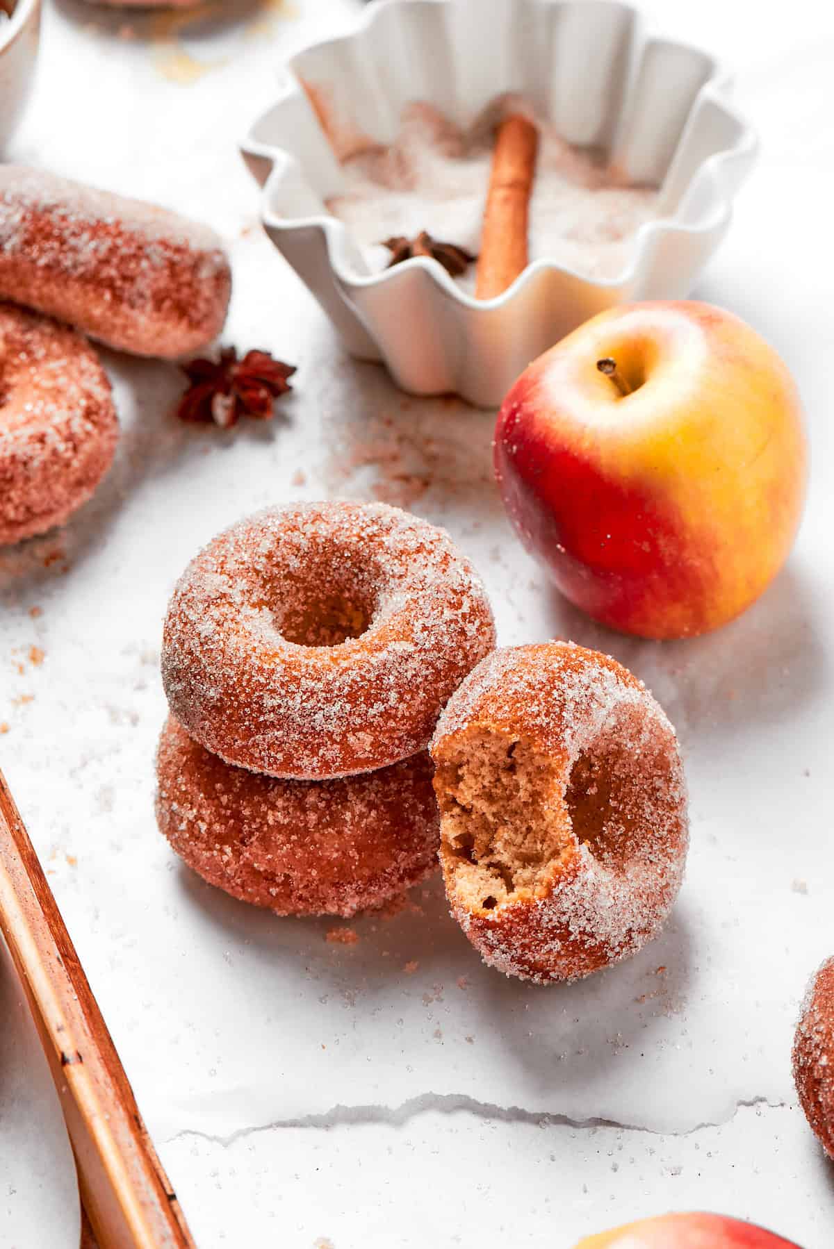 A little stack of apple cider donuts next to an apple.