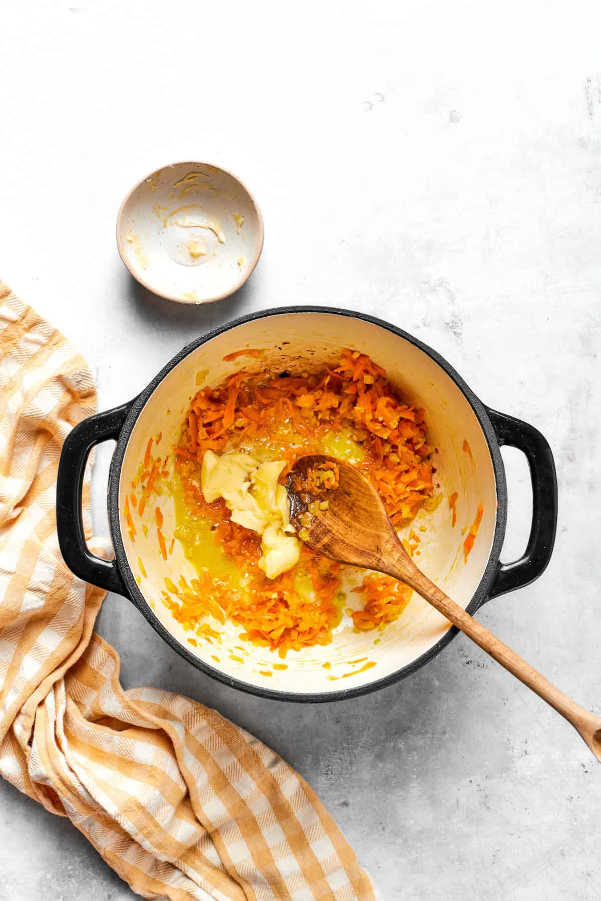 Adding butter to a pot with shredded carrots.