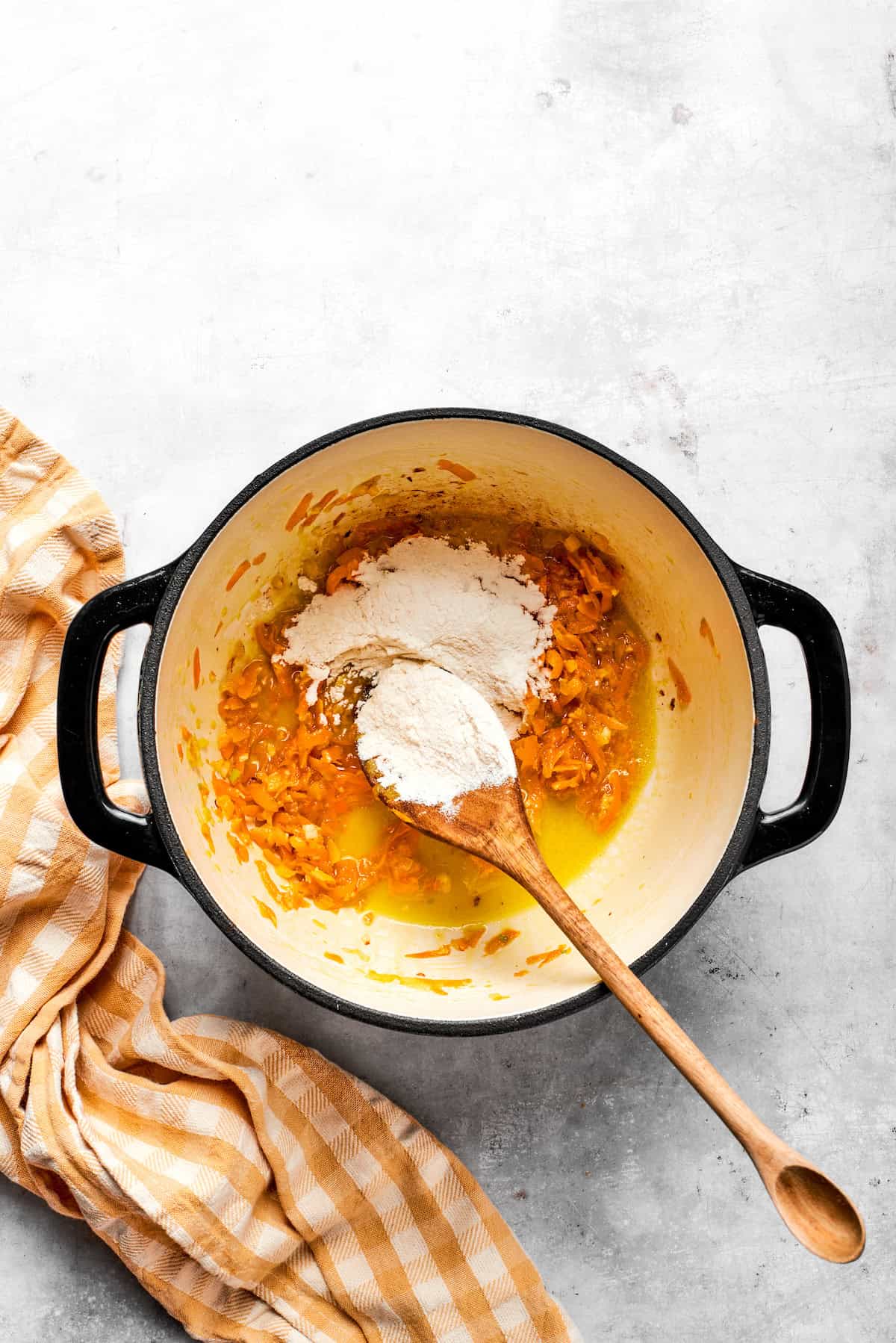 Adding flour to a pot with carrots and butter.