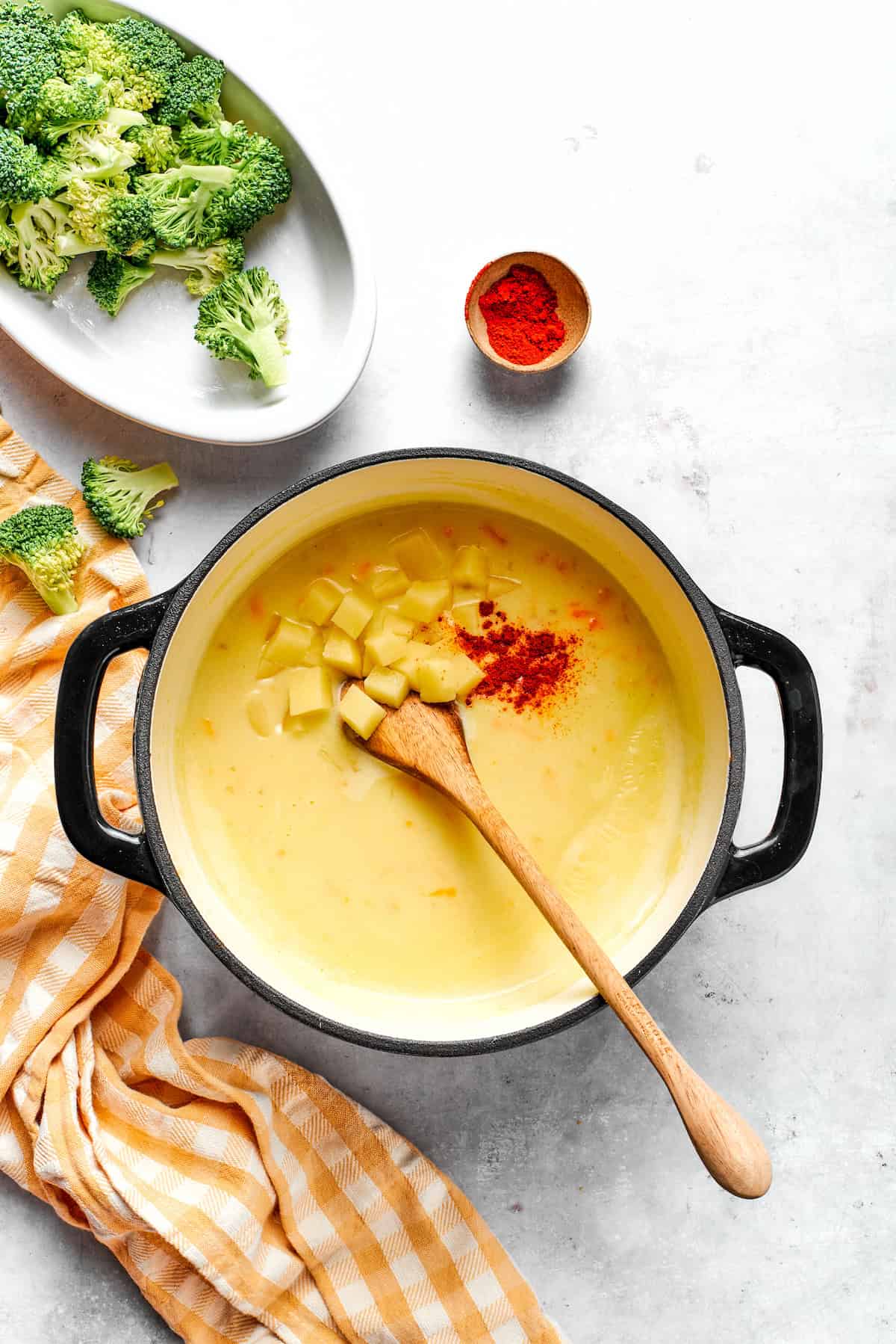 Adding diced potato and paprika to soup in a pot.