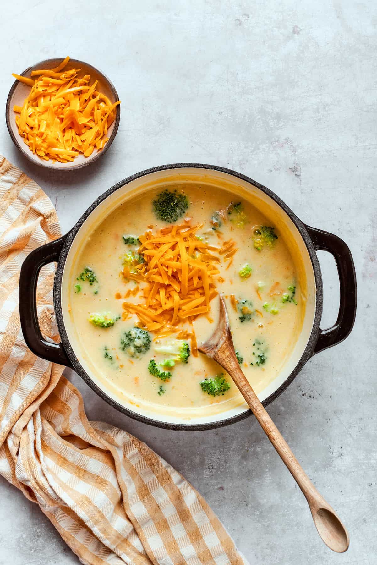 Adding shredded cheddar to a pot with soup.