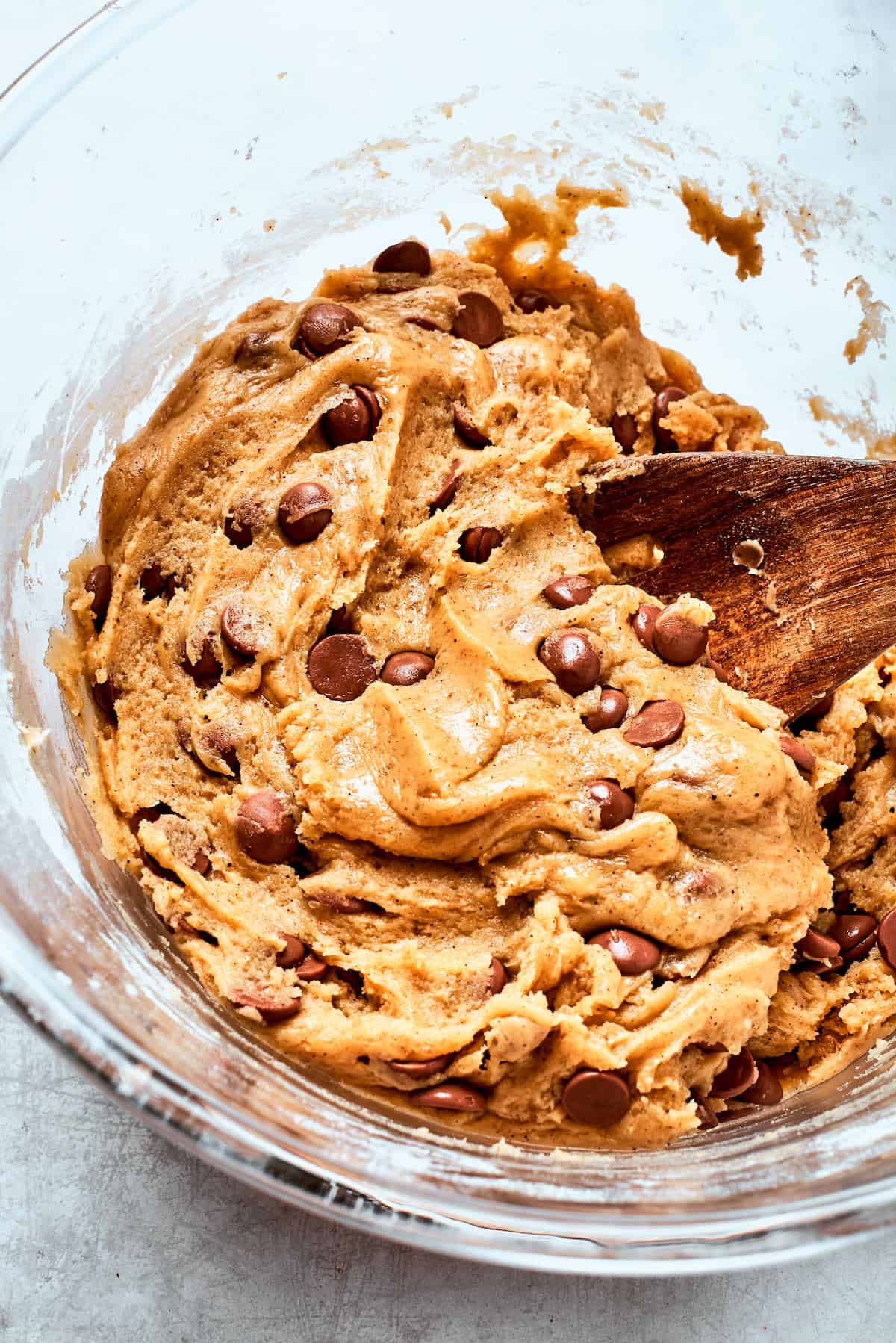 A wooden spoon stirs a bowl of chocolate chip cookie dough.