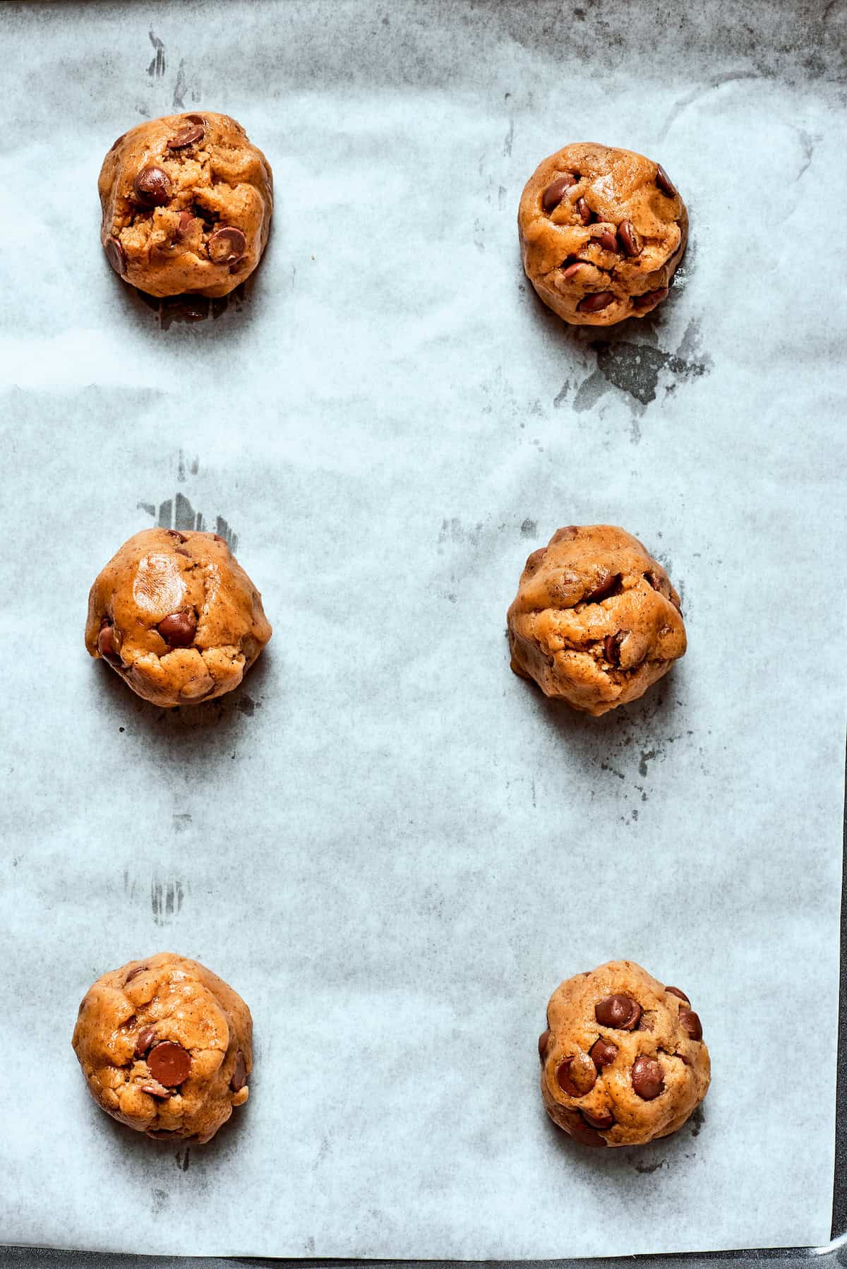 Balls of brown butter chocolate chip cookie dough on a lined baking sheet.