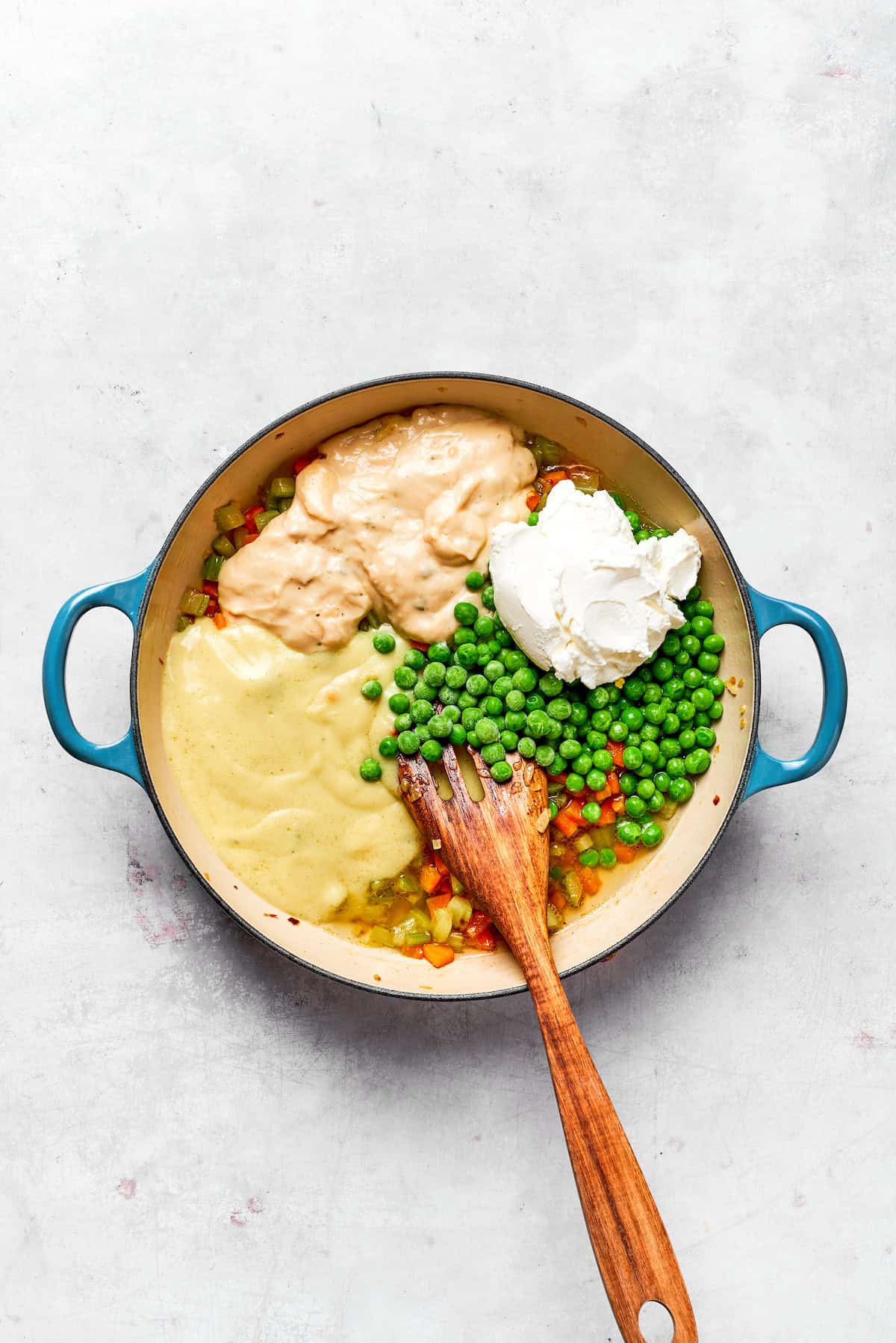 Adding sour cream, condensed soups, and peas to a pot.